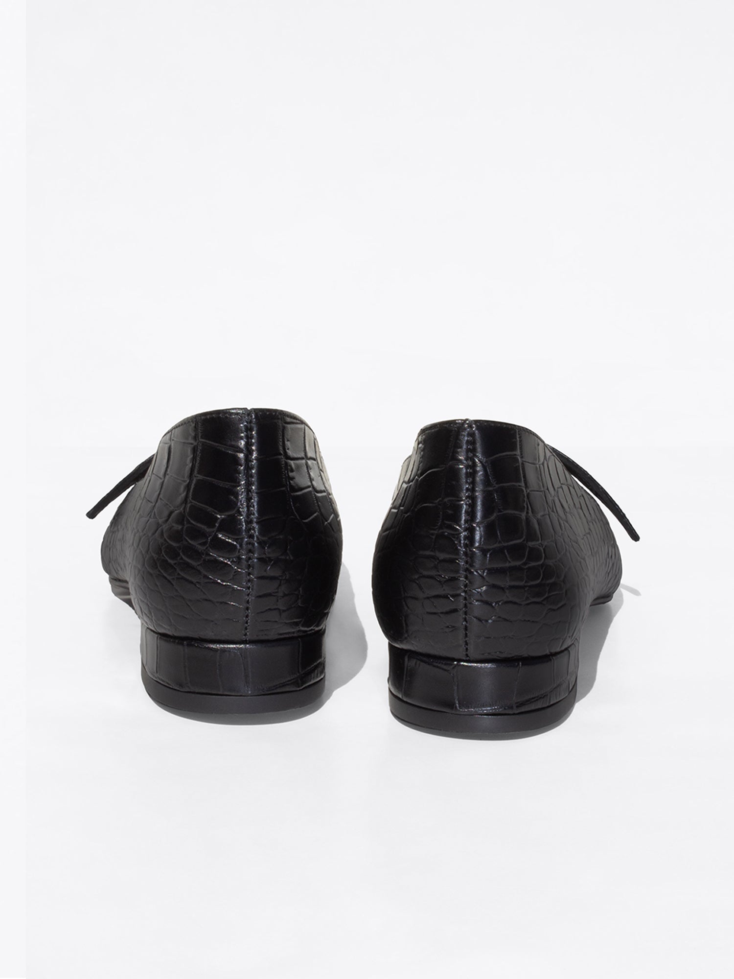Black crocodile-embossed leather flats shown from the back, with a low block heel