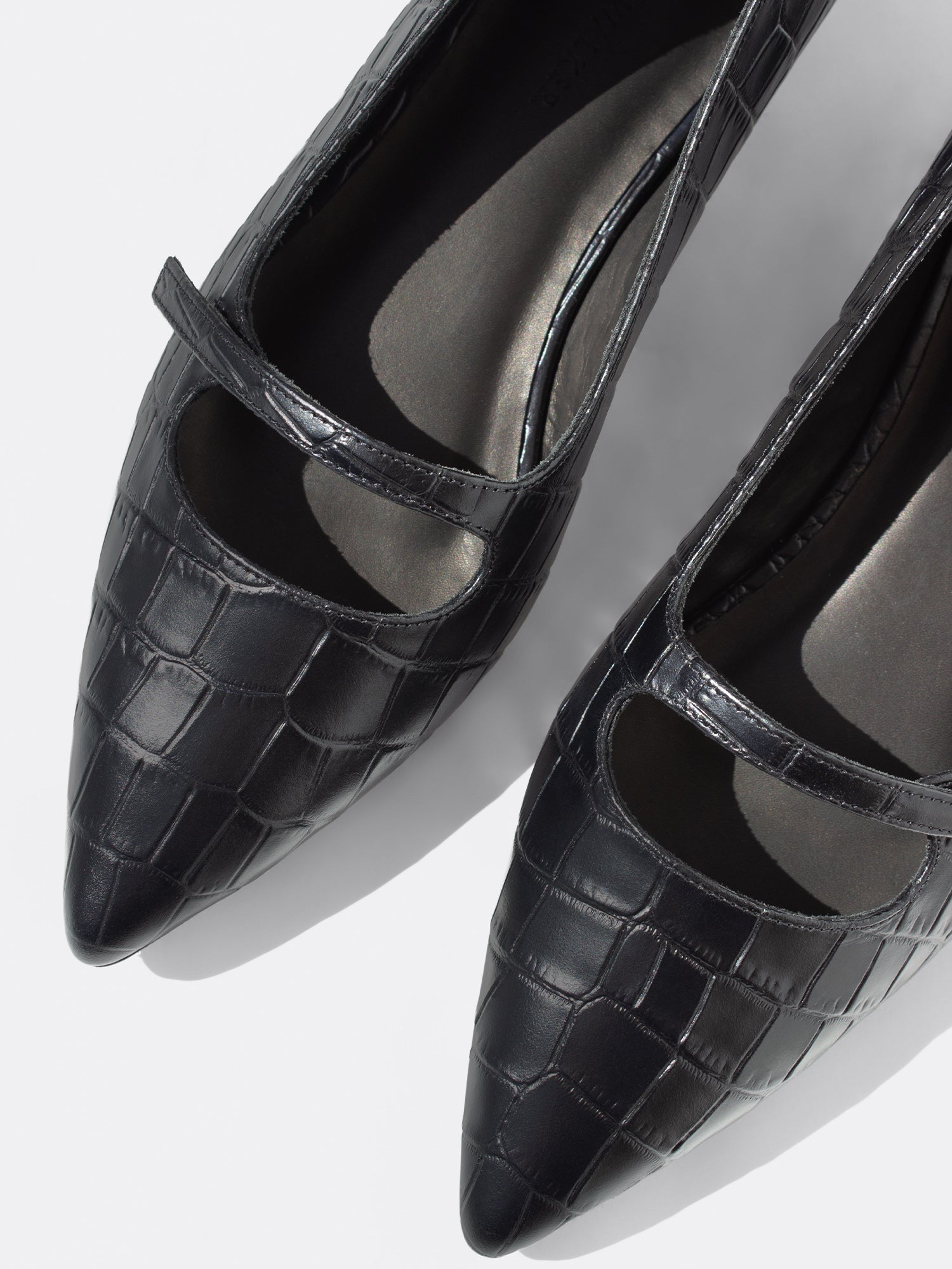 Black crocodile-embossed leather pumps with pointed toe and mary-jane strap, close-up top-down shot