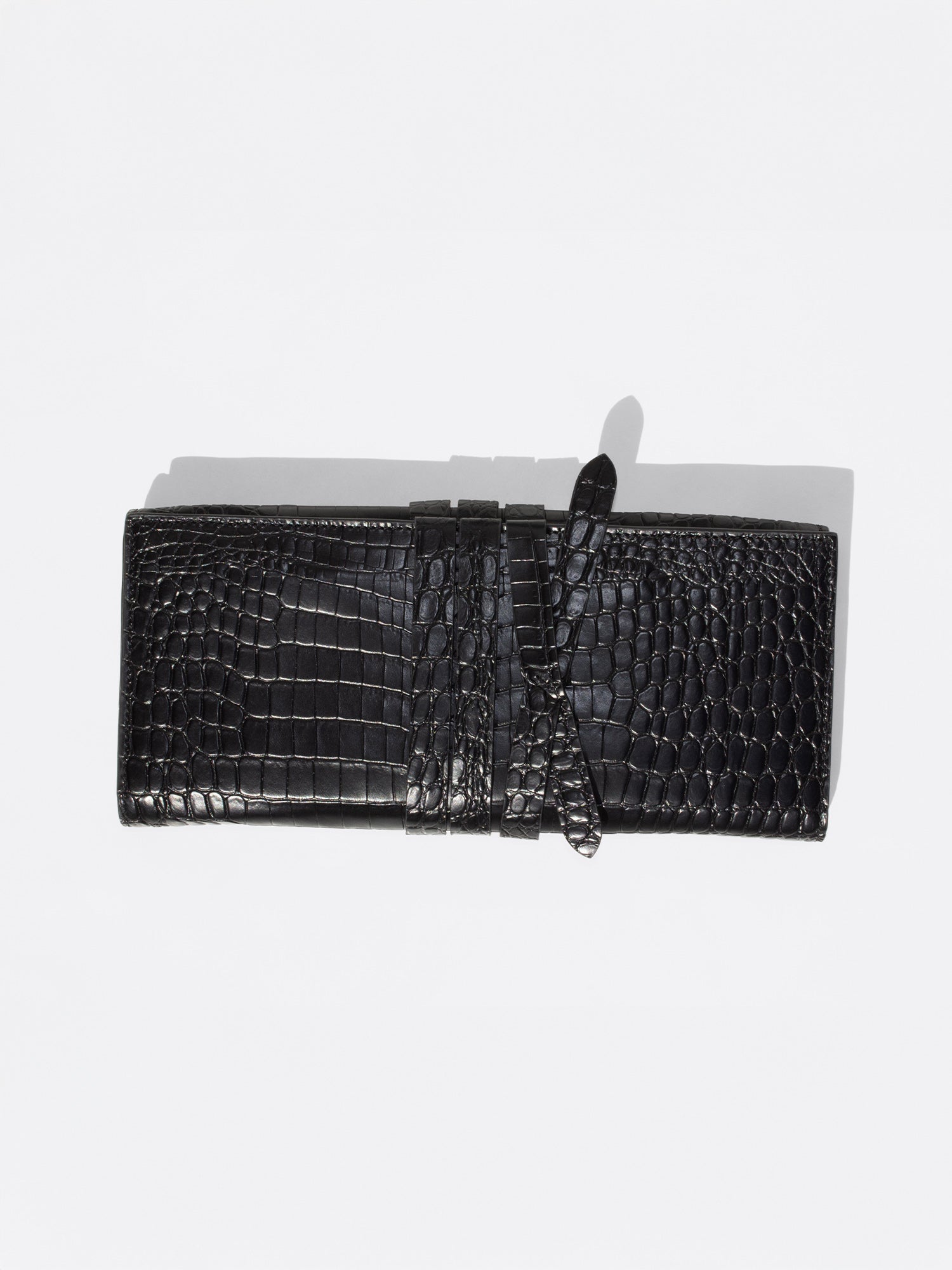 Black crocodile-embossed leather clutch with wrap-around strap detail, flat top-down product shot