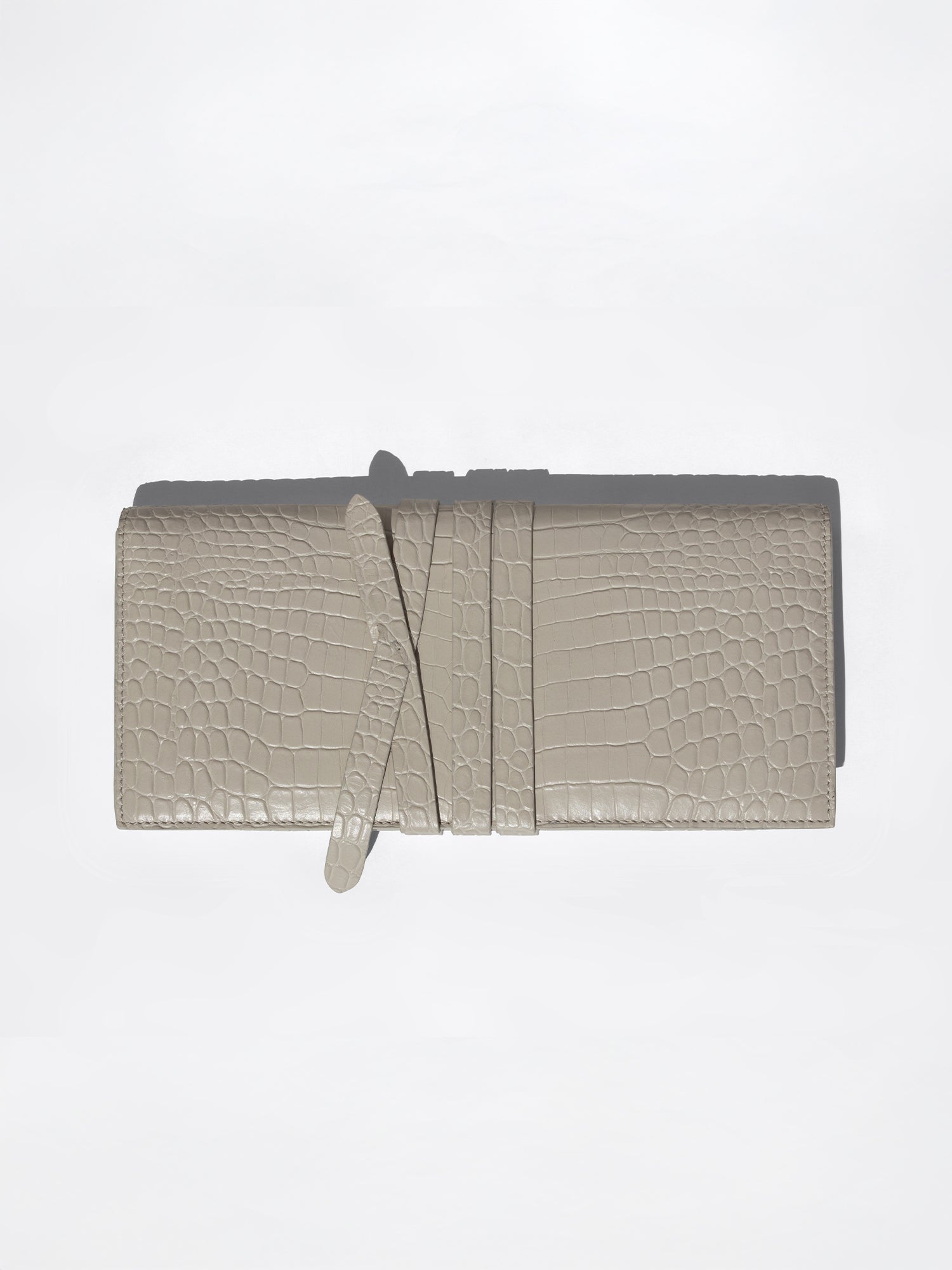 Light taupe crocodile-embossed leather clutch wallet with wrap-around strap closure, flat product shot