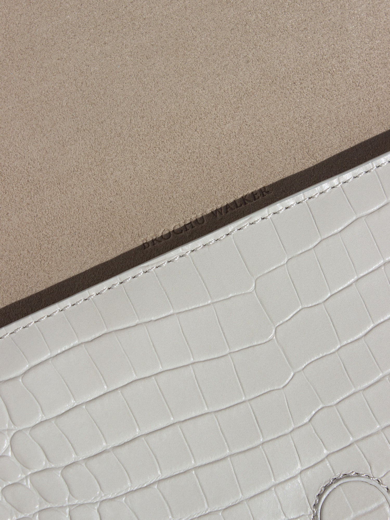Close-up of a white crocodile-embossed leather clutch with beige suede lining and Brochu Walker branding