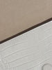 Close-up of a white crocodile-embossed leather clutch with beige suede lining and Brochu Walker branding