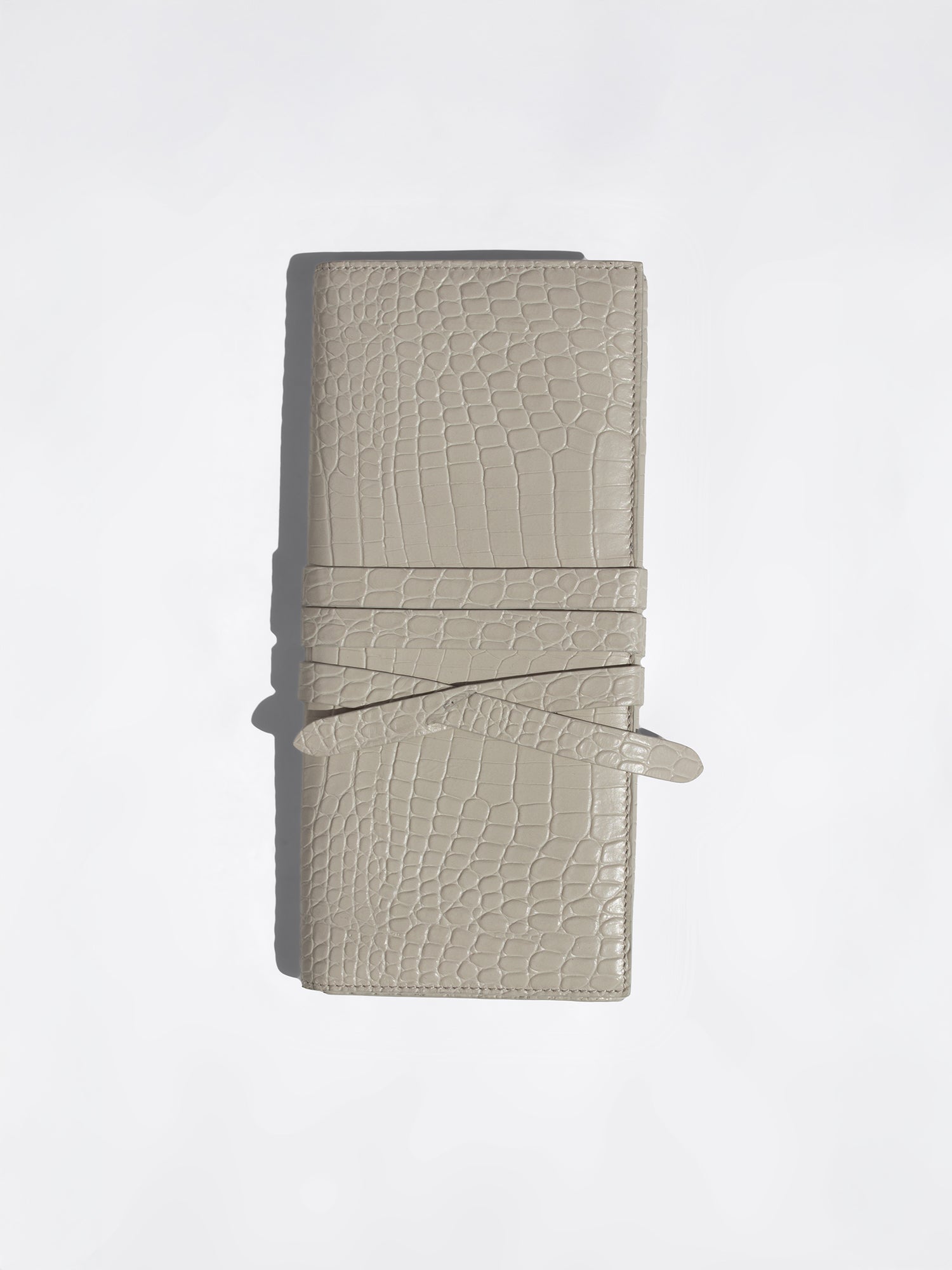 Light beige crocodile-embossed leather wallet with wrap-around strap closure, flat product shot