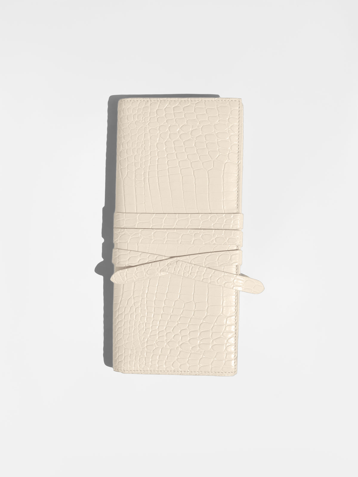 Ivory croc-embossed leather clutch bag closed with its wrap-around tie strap