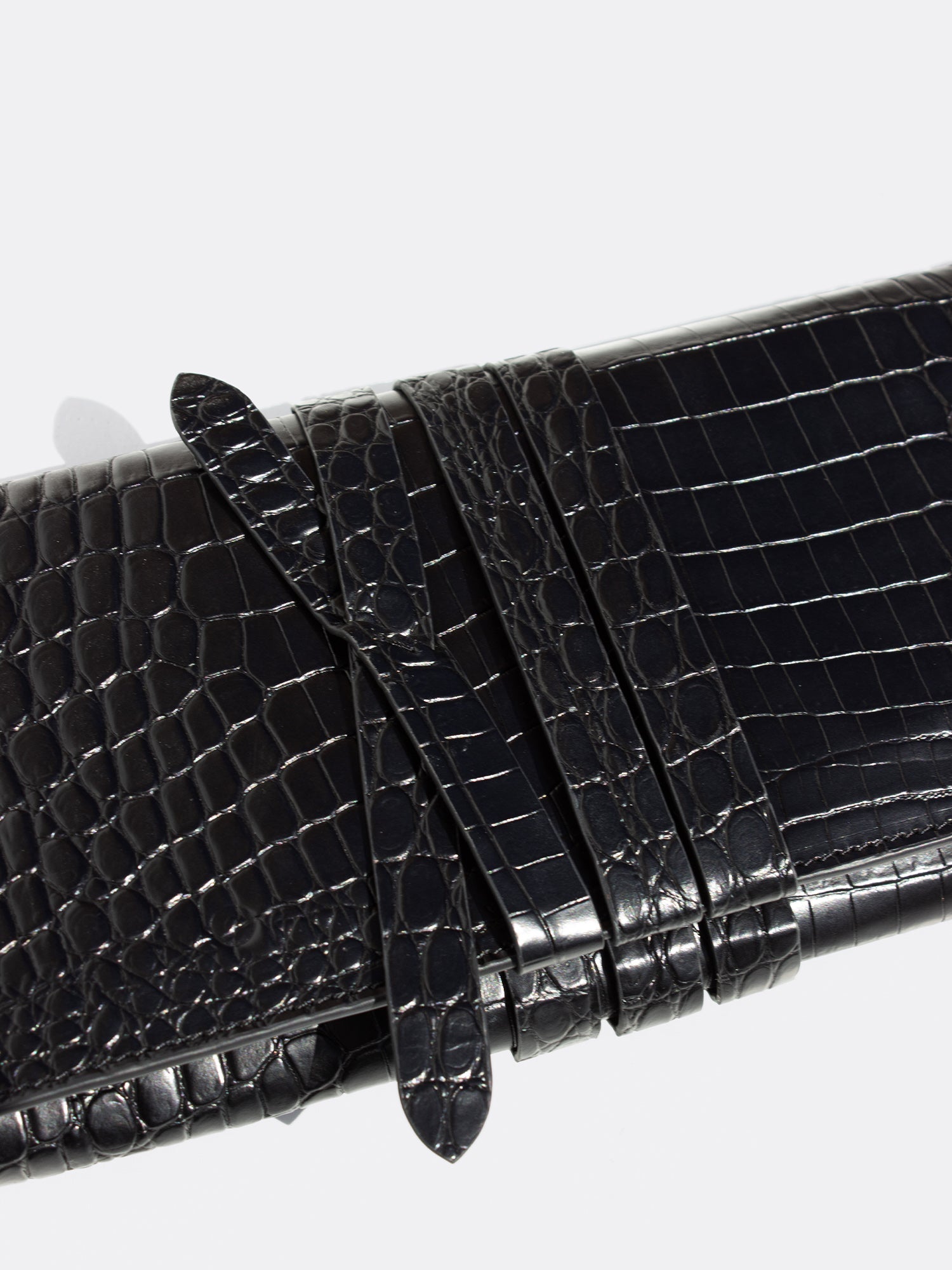Close-up of a black crocodile-embossed leather clutch with wrap-around strap detail