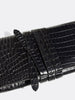 Close-up of a black crocodile-embossed leather clutch with wrap-around strap detail