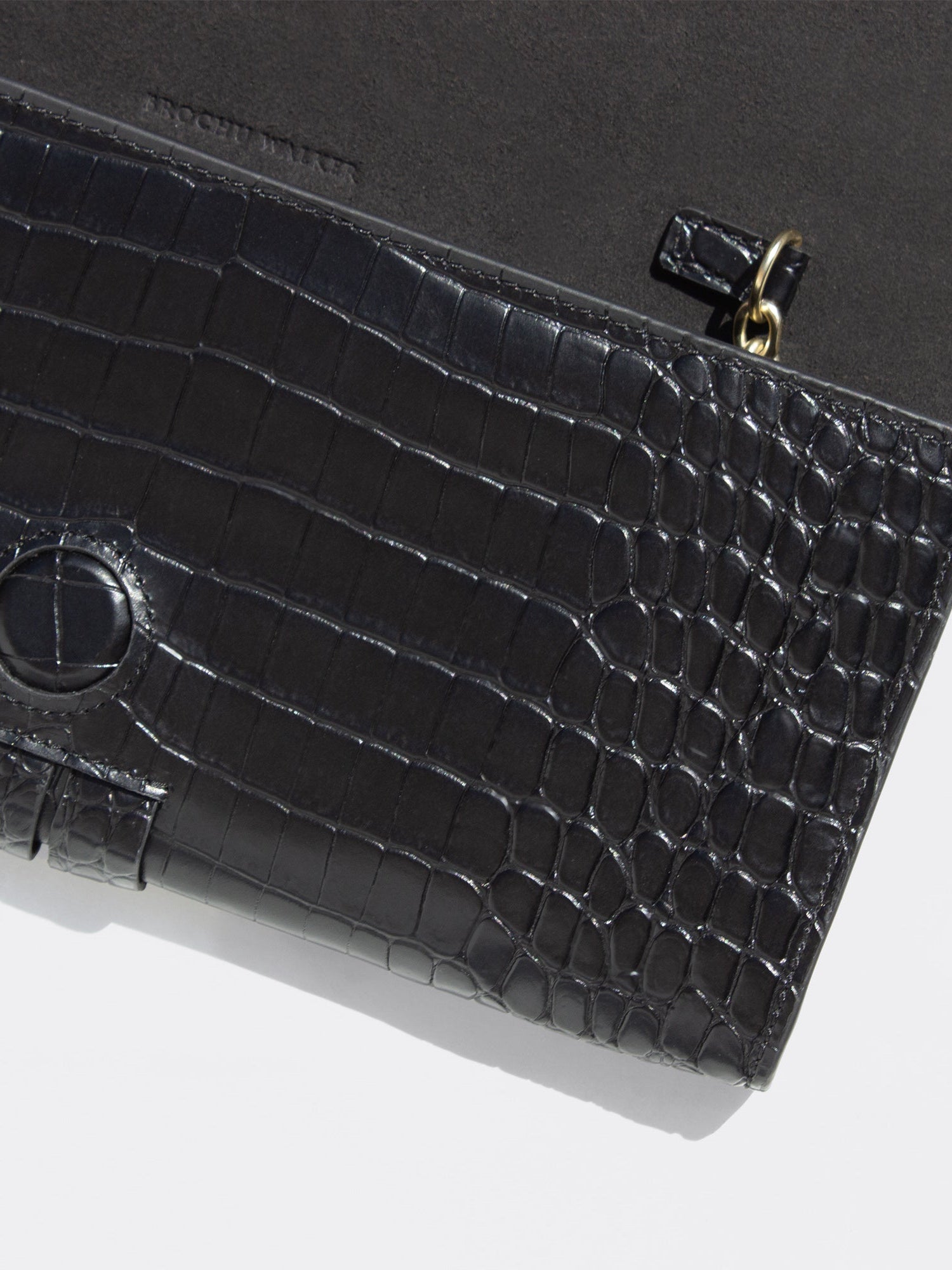 Close-up of a black crocodile-embossed leather clutch with gold ring pull detail