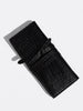 Black crocodile leather clutch bag shown at an angle with its wraparound tie strap, cast shadow on light gray background