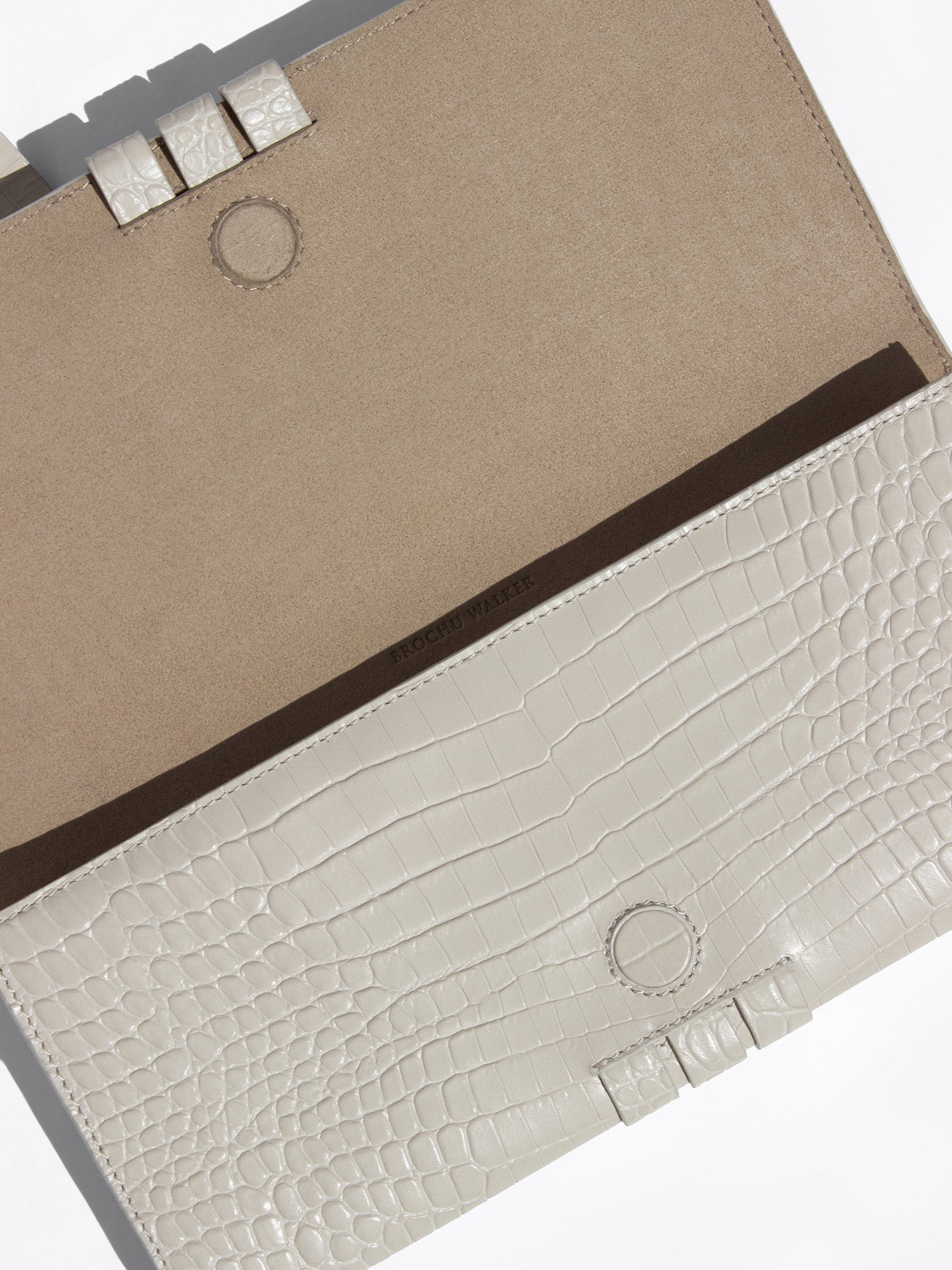 Close-up of a structured clutch bag in warm beige and off-white textured leather with dark brown trim
