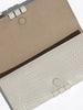 Close-up of a structured clutch bag in warm beige and off-white textured leather with dark brown trim