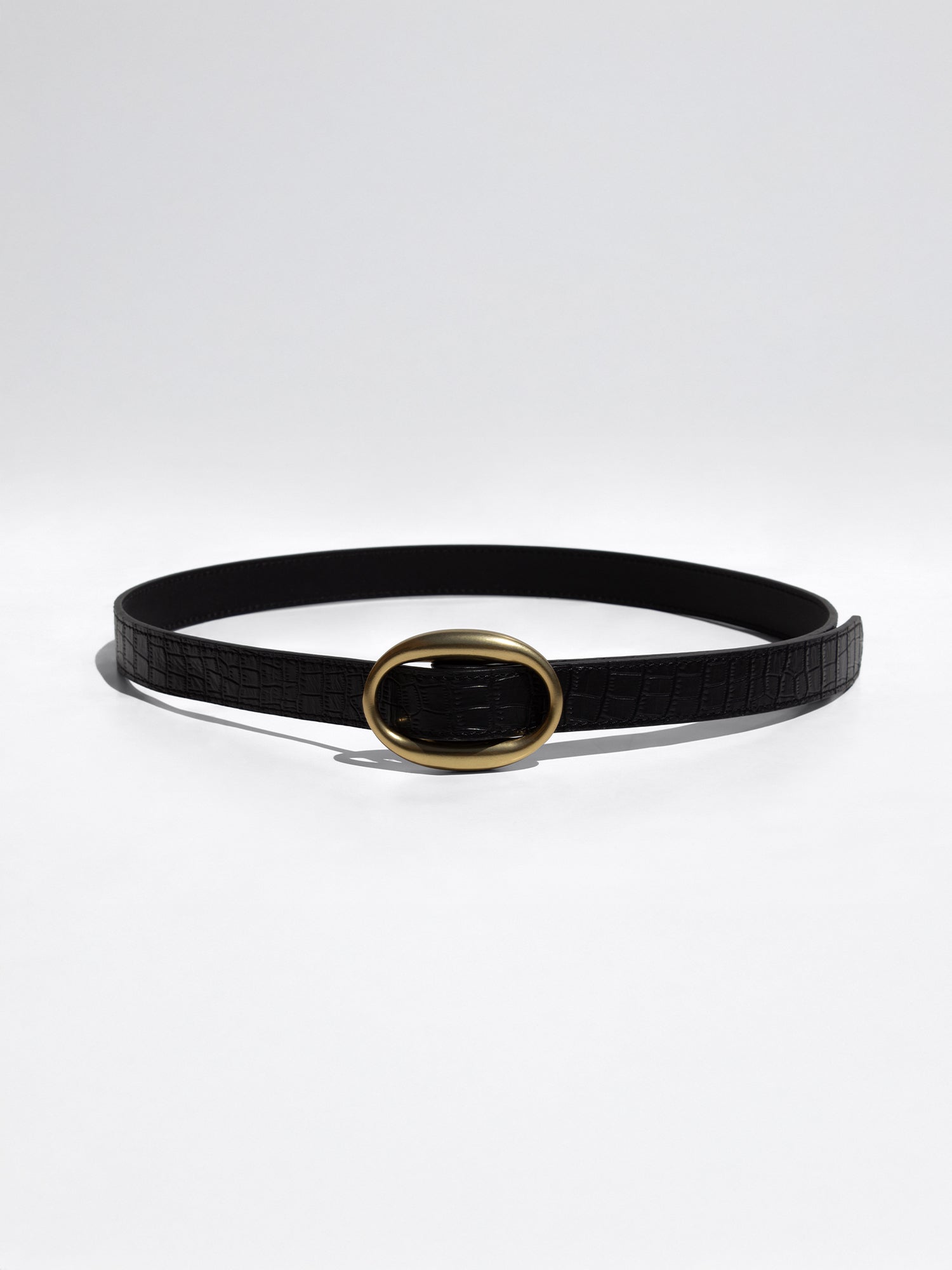 Black crocodile-embossed leather belt with a gold oval buckle, coiled on a plain white background