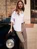 White shirt for women styled with beige trousers, worn outdoors next to a classic black car.