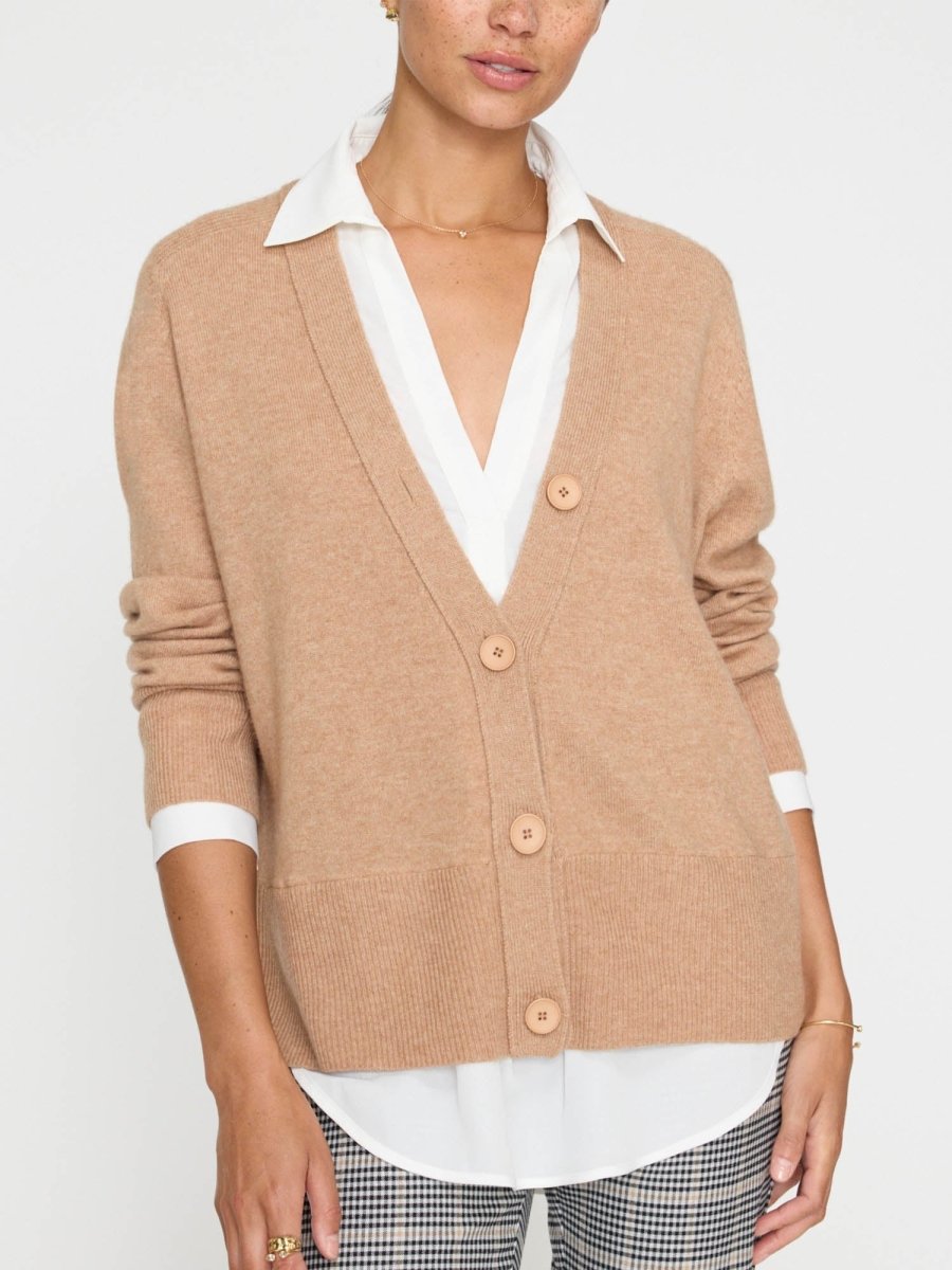 Women's camel cardigan with button front, layered over a white collared shirt and paired with plaid trousers.