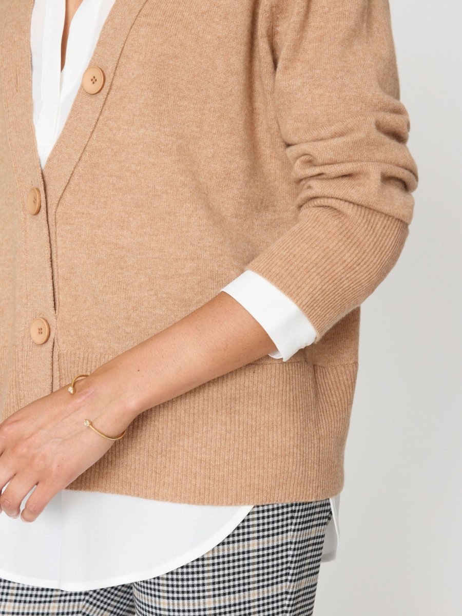 Designer cardigan for women in camel with large buttons, layered over a white shirt and paired with plaid pants.