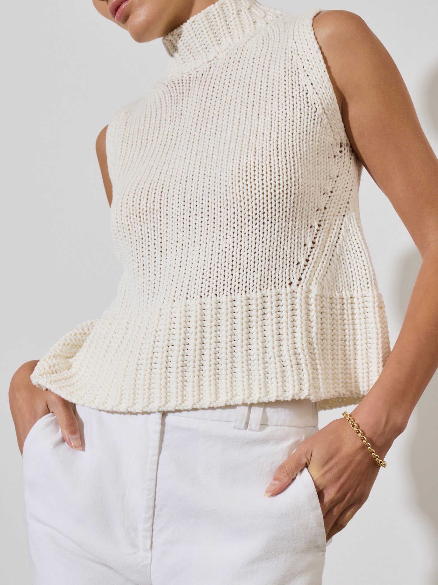 White knitted tank top for women featuring a high ribbed neckline and relaxed fit paired with dark trousers.