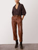 Woman wearing a dark brown blouse with balloon sleeves tucked into brown leather ankle pants with a belt and dark suede boots