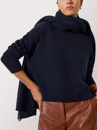 Navy cashmere fringe wrap draped over a matching sweater, styled with brown leather pants.