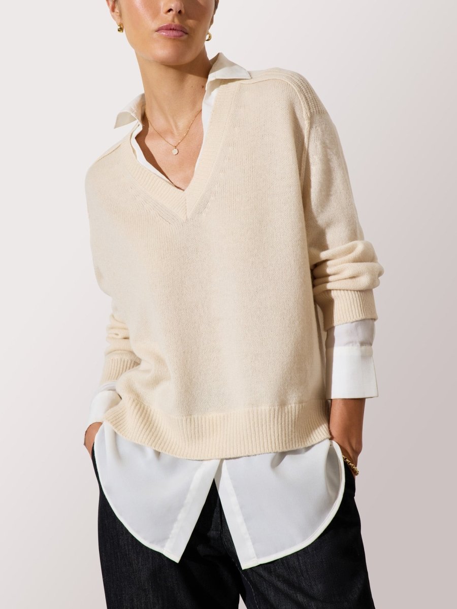 Women's layered collared shirt under sweater styled with a beige V-neck knit and dark wide-leg pants.