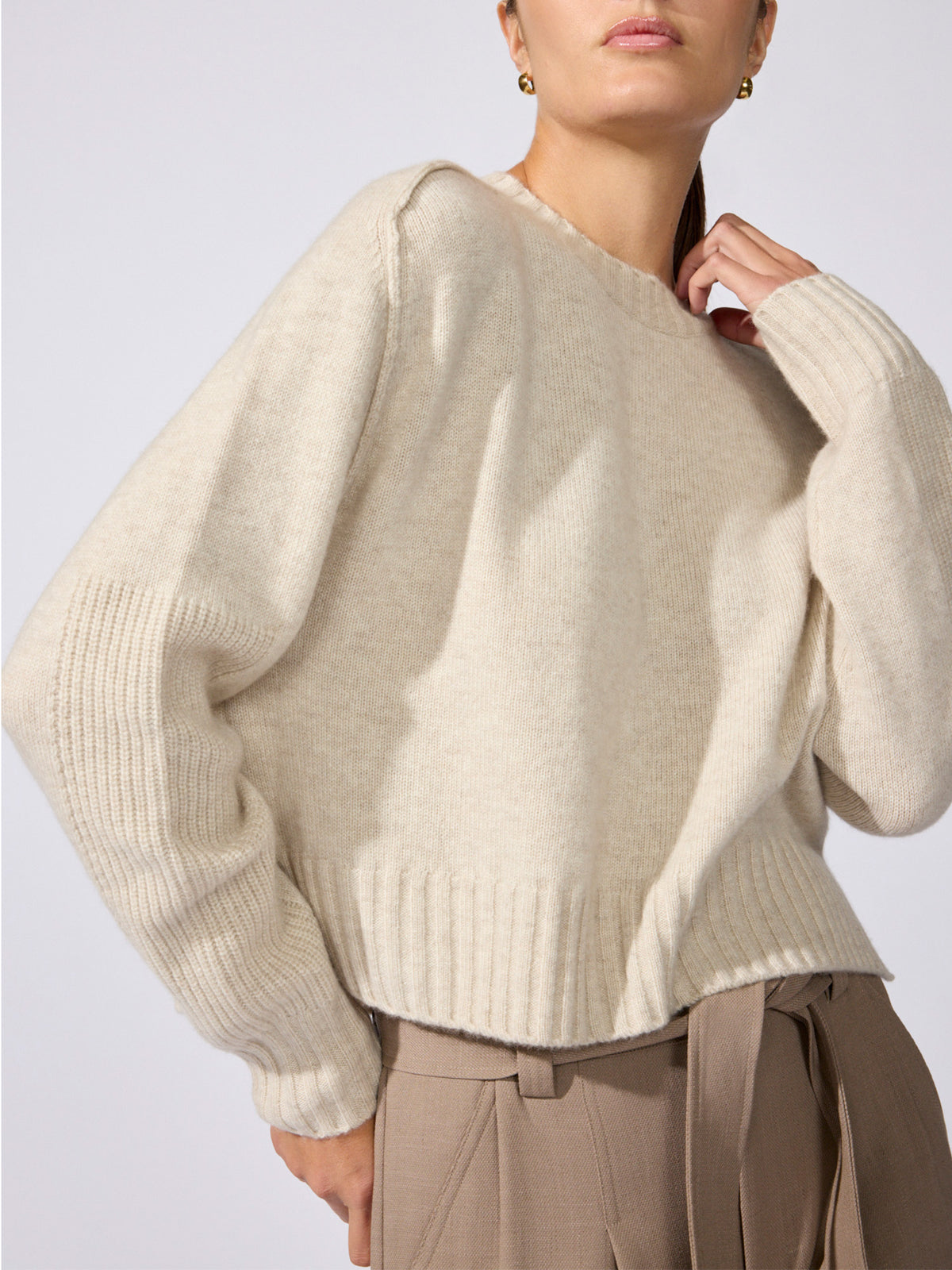 Woman wearing a cream cashmere crewneck sweater with ribbed trim and taupe trousers