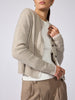 Side profile of a woman wearing the Archie layered cardigan in gravel stone melange, open over a white ribbed top with beige trousers.