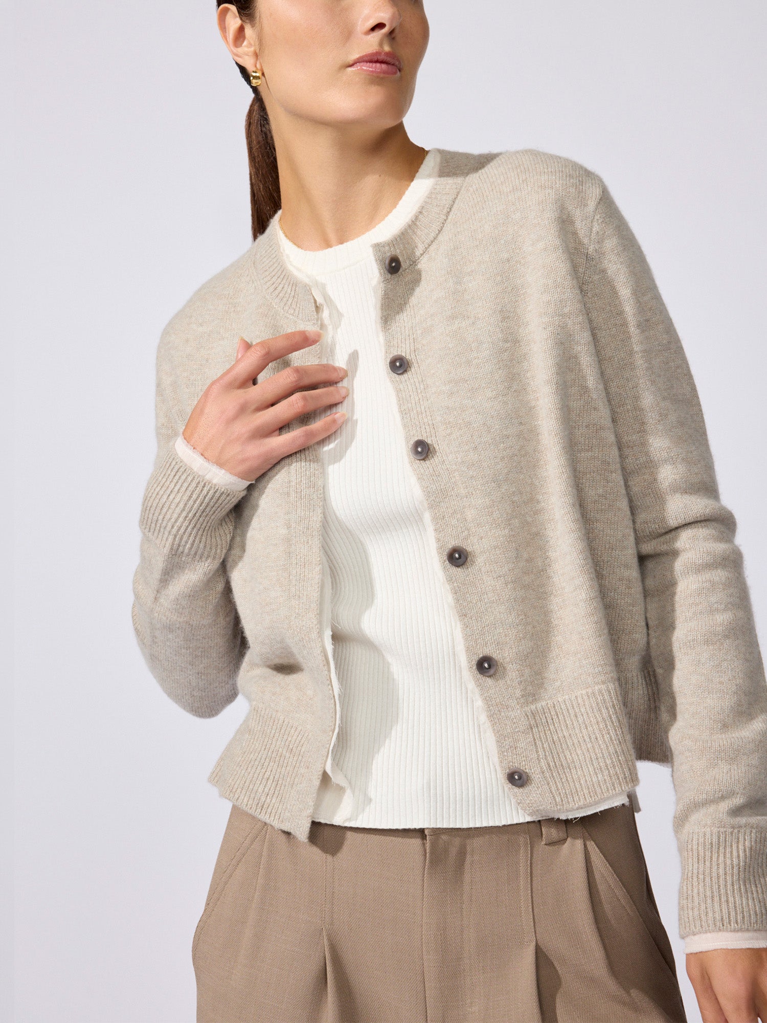 Woman wearing the Archie layered cardigan in gravel stone melange over a white ribbed top, paired with beige trousers.