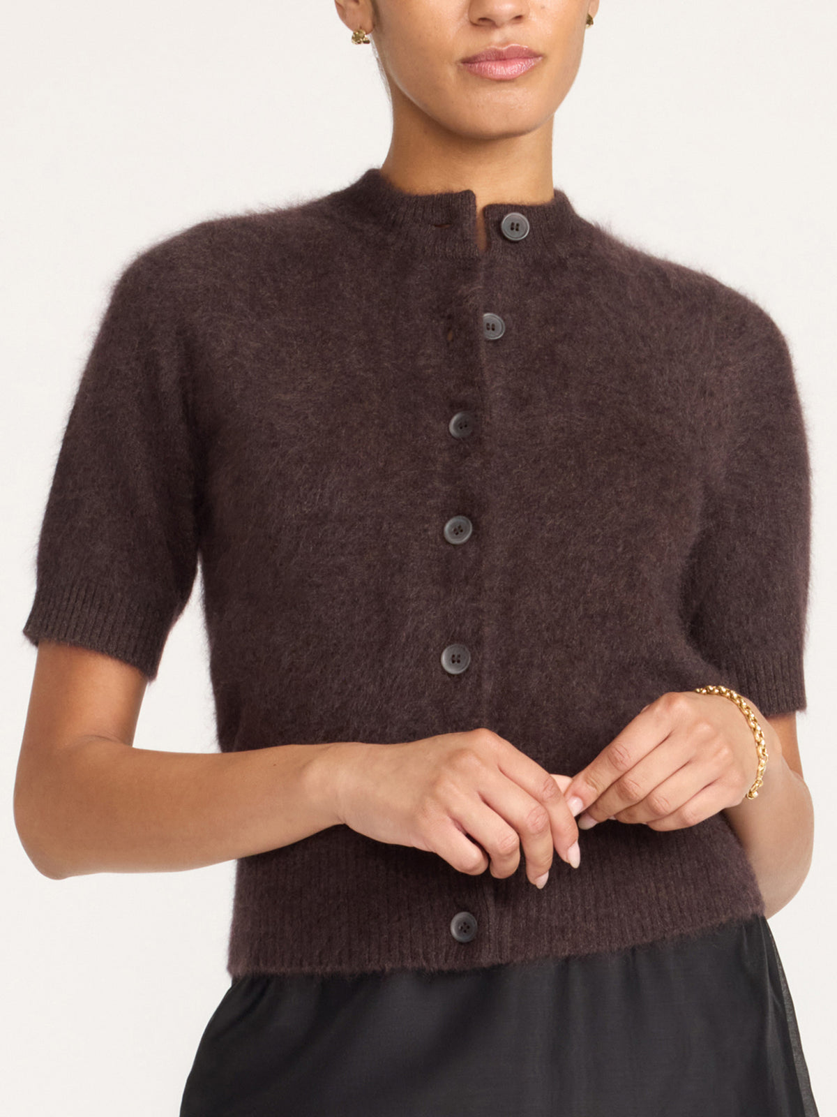Women's brown cashmere cardigan with short sleeves and dark buttons, worn with a black skirt and a gold bracelet