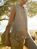 Classy sleeveless top in natural linen with a V-neckline and relaxed fit worn outdoors with matching trousers and a tan suede tote bag.