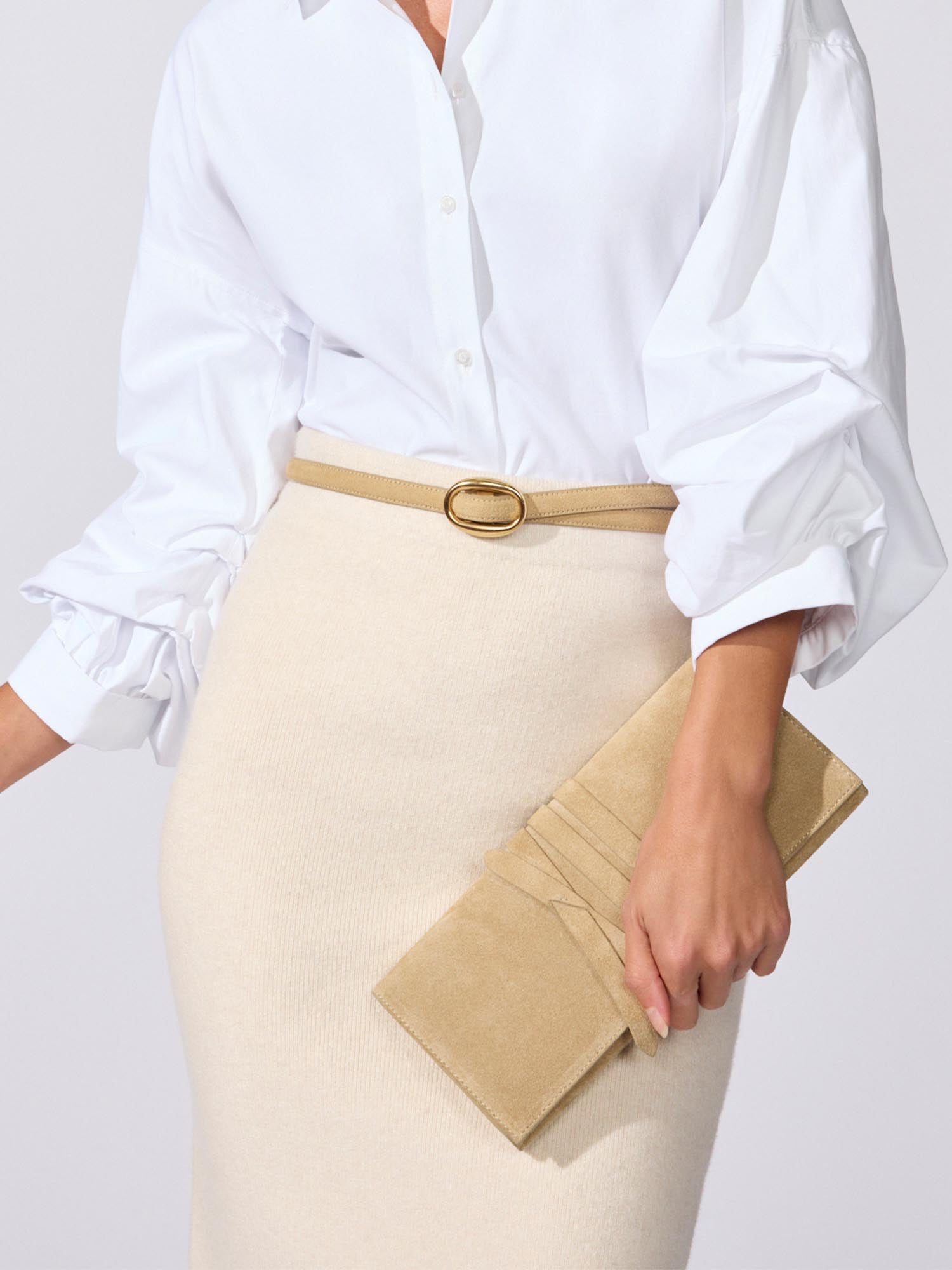 Close-up of a white ruffled-sleeve blouse tucked into a beige pencil skirt with a tan belt, holding a tan clutch bag.