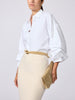 Woman wearing the Eliana shirt in salt white with a beige belt, paired with a cream pencil skirt and beige clutch