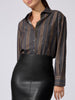 Woman wearing a charcoal striped button-down shirt with brown and gold vertical stripes, paired with a black faux-leather skirt.