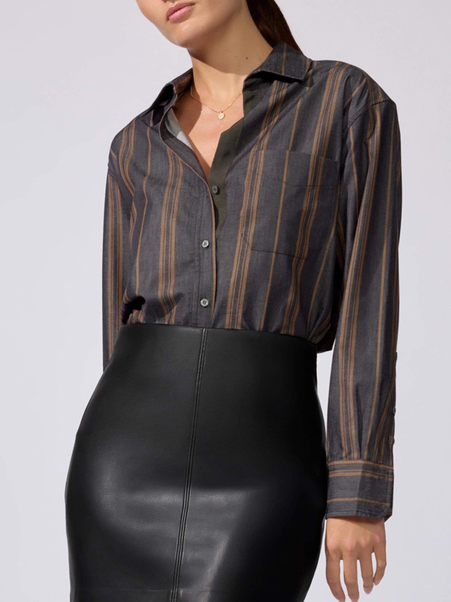 Woman wearing a charcoal striped button-down shirt with brown and gold vertical stripes, paired with a black faux-leather skirt.