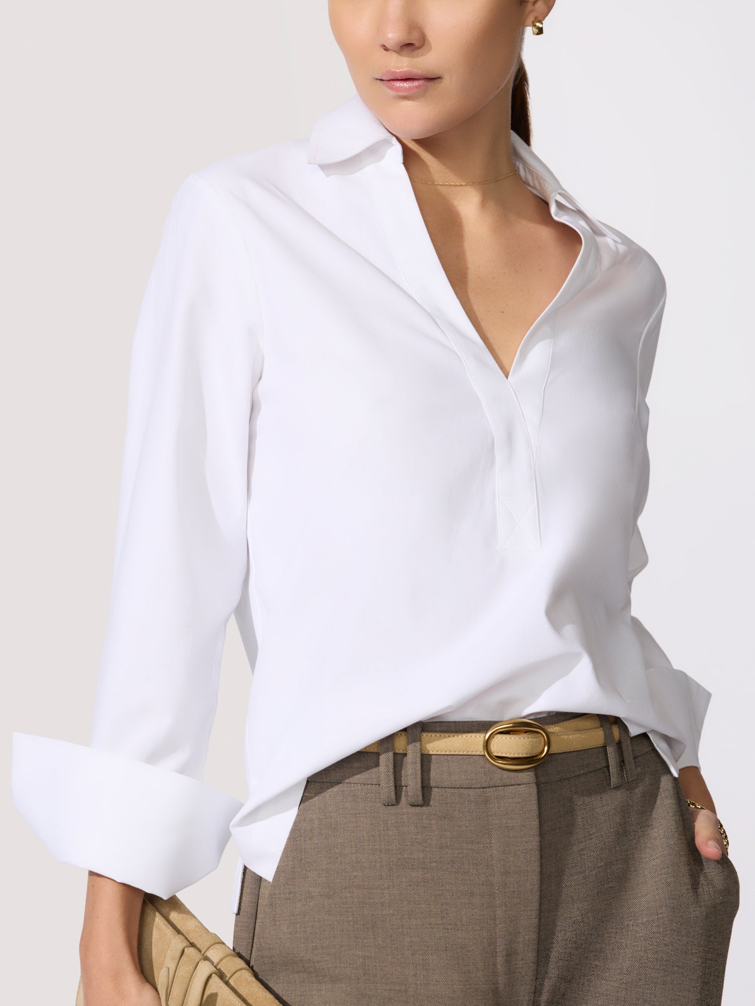 Classy white top in a crisp poplin with a spread collar, V-neckline, and long cuffed sleeves tucked into taupe trousers with a tan oval-buckle belt.