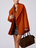 Woman wearing the oversized Finley wrap coat in canyon orange multi with a gray shirt and black leather mini skirt, holding a brown suede duffel bag