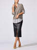 Woman wearing the V-neck pullover in otter melange with flint stripe over a striped shirt, paired with a black faux-leather midi skirt and beige heels.