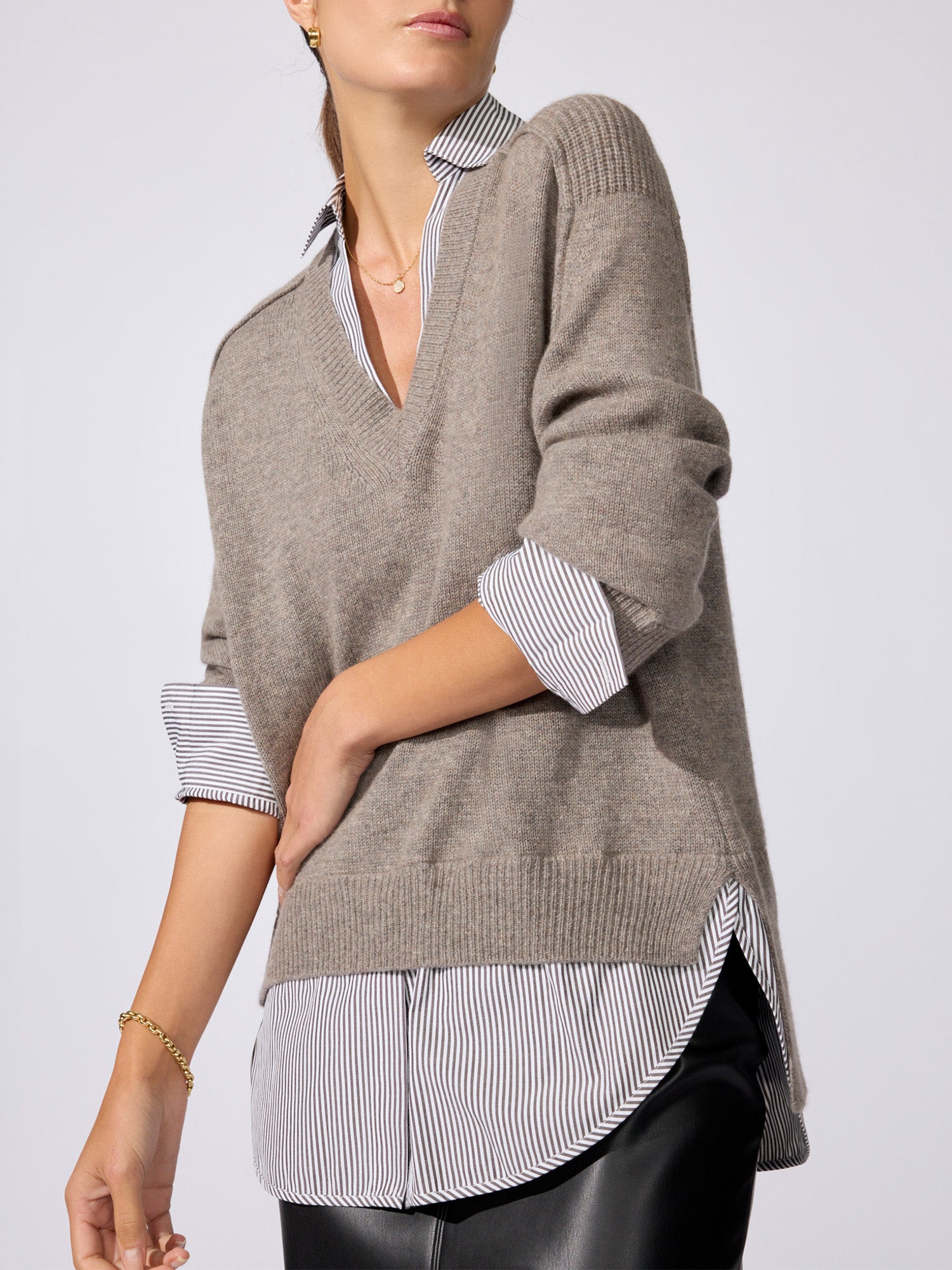 Close-up side view of the V-neck pullover in otter melange with flint stripe, showing the ribbed hem layered over a striped button-down shirt.