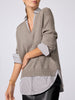 Close-up side view of the V-neck pullover in otter melange with flint stripe, showing the ribbed hem layered over a striped button-down shirt.