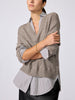Woman wearing the V-neck pullover in otter melange with flint stripe, arms crossed over a striped shirt with black pants.