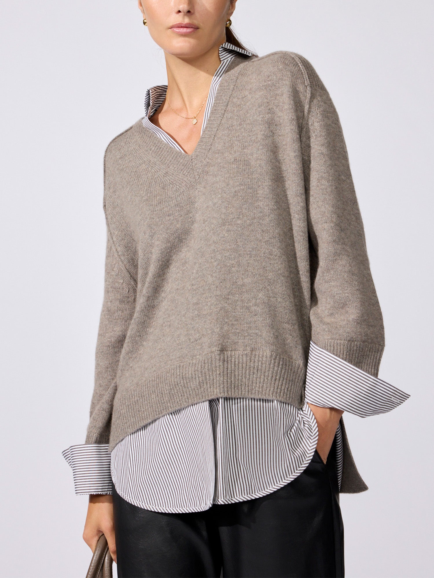 Woman modeling the oversized V-neck pullover in otter melange with flint stripe, worn over a striped button-down shirt with black pants.