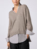 Woman modeling the oversized V-neck pullover in otter melange with flint stripe, worn over a striped button-down shirt with black pants.