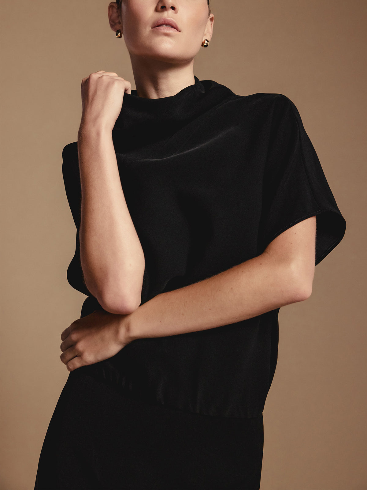 Woman wearing a black funnel neck dress with short sleeves, posed against a tan studio background