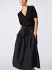 Woman wearing the Isola dress in black onyx, featuring a collared top and a high-waisted pleated skirt with a tie waist