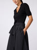 Woman wearing the Isola dress in black onyx, styled with a wrap-front top and wide-leg silhouette and a tie waist