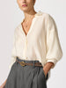 Woman wearing an off-white linen button-up blouse tucked into gray trousers with a brown belt