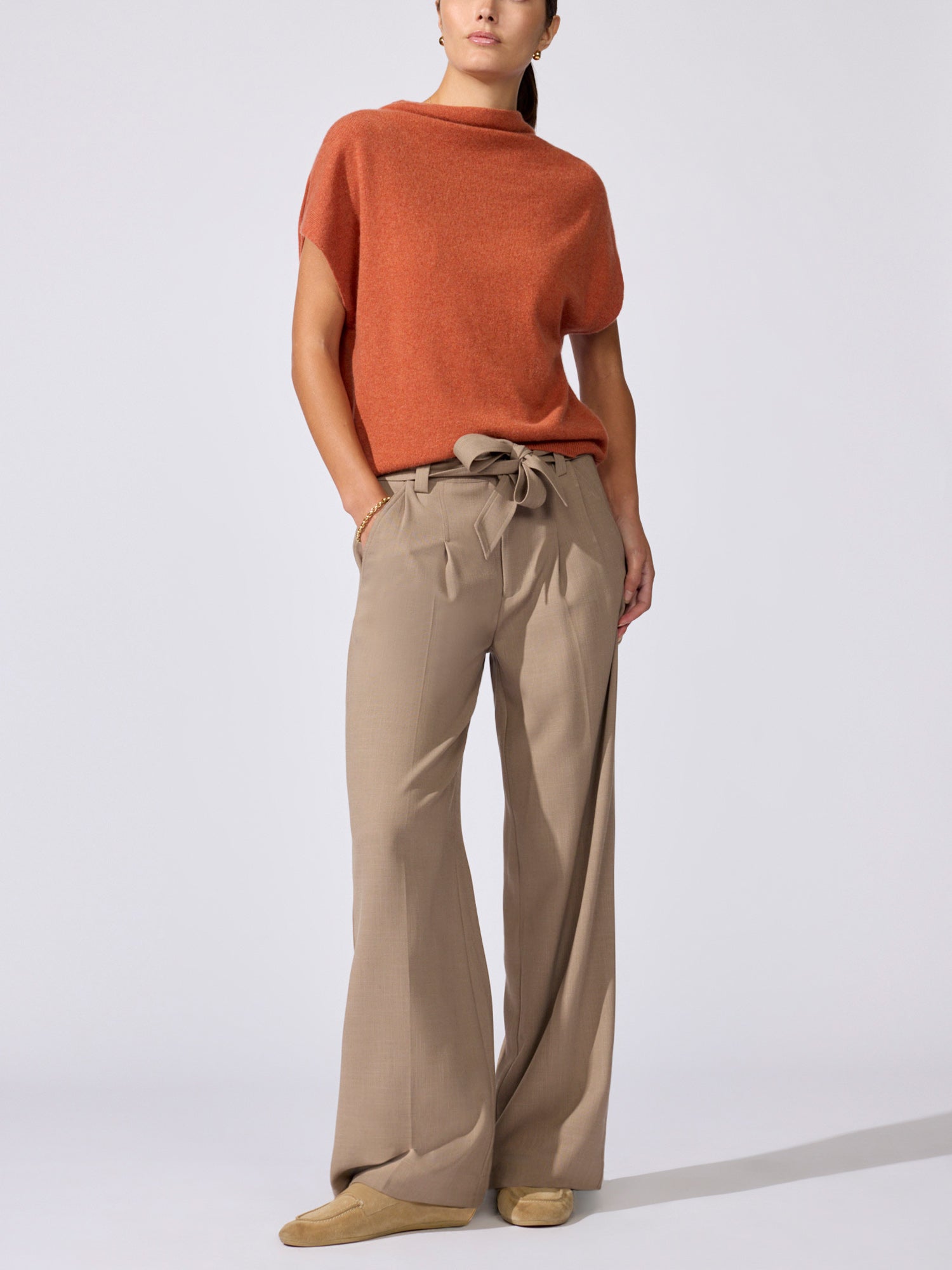 Woman wearing the Morten funnel neck cashmere top in canyon orange melange with beige wide-leg drawstring trousers, standing