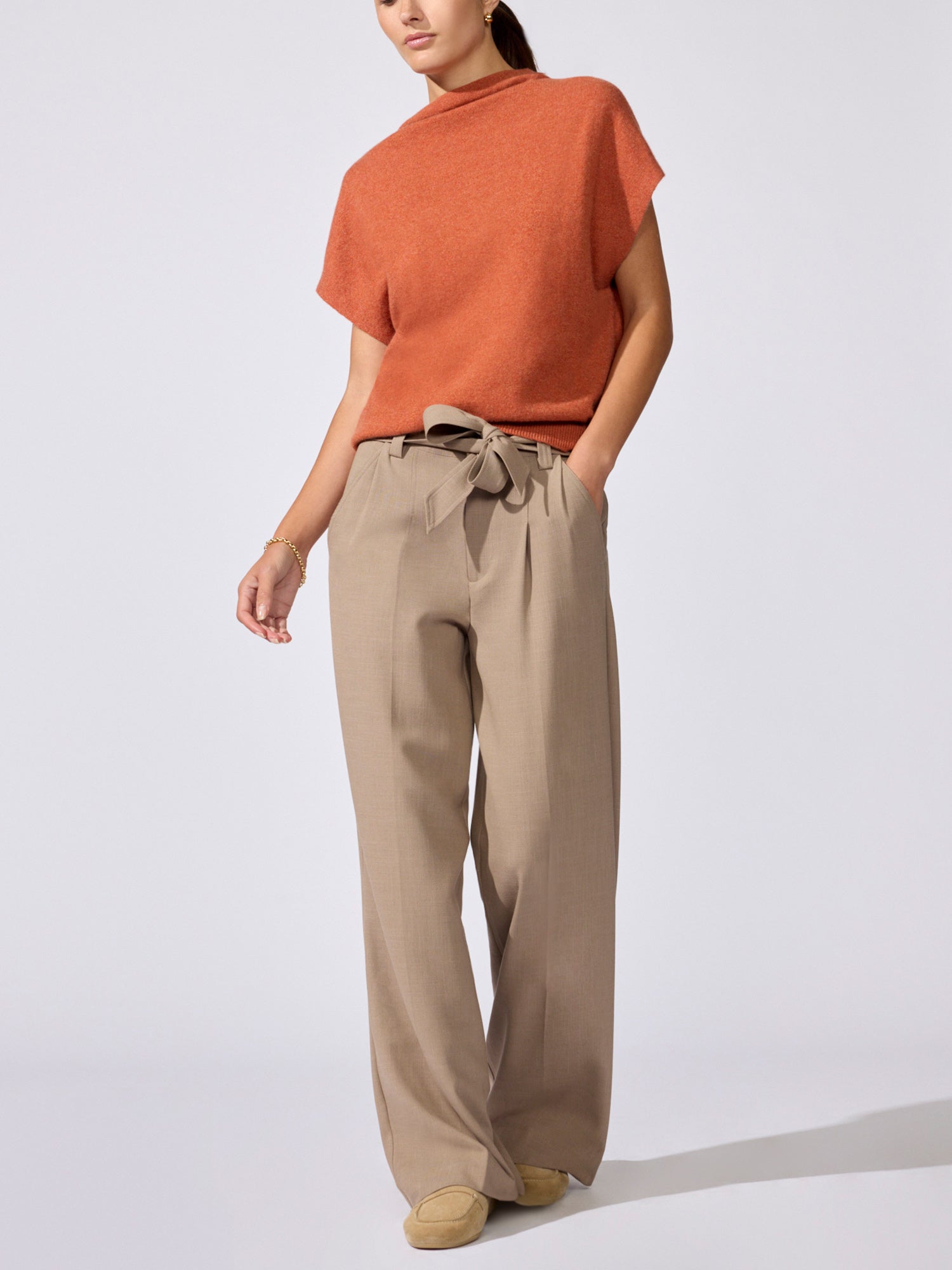 Full-length view of the Morten funnel neck cashmere top in canyon orange melange with beige wide-leg trousers