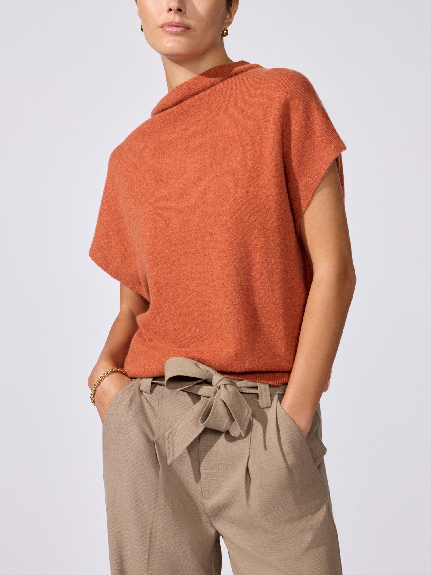 Woman modeling the Morten funnel neck cashmere top in canyon orange melange with beige tie-waist trousers