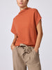 Woman modeling the Morten funnel neck cashmere top in canyon orange melange with beige tie-waist trousers