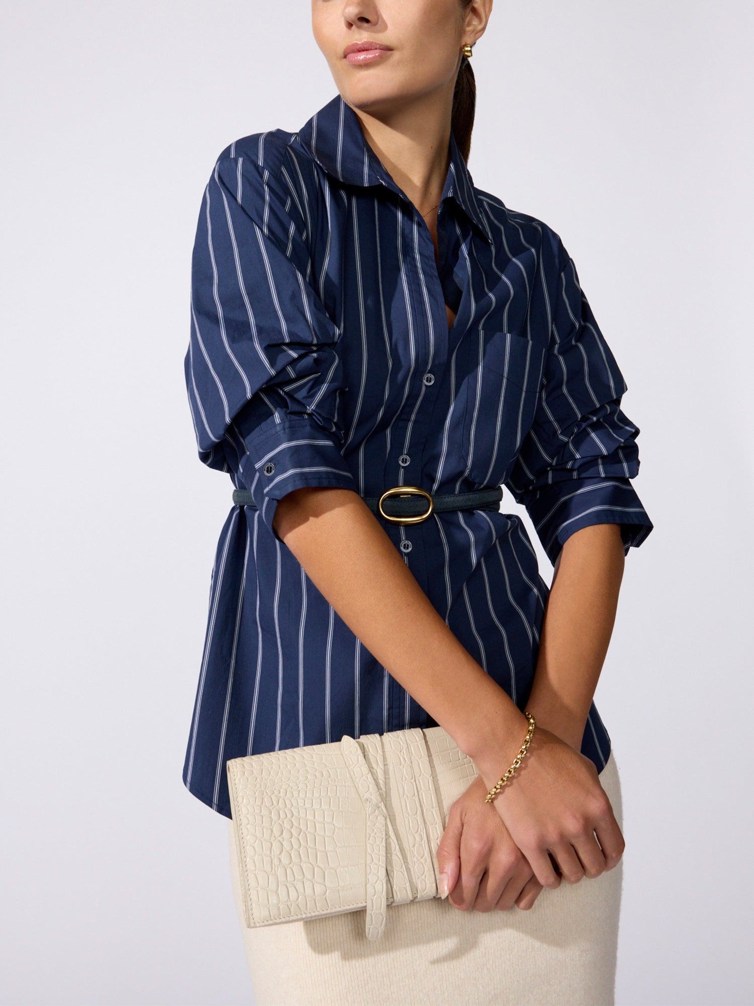 Close-up of a woman wearing a navy pinstripe shirt with a black woven belt, holding a cream clutch bag