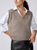 Woman wearing a taupe V-neck knit sweater vest over a white collared shirt, paired with black leather trousers.