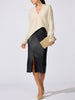 Woman wearing a cream V-neck sweater with a black leather midi skirt and a beige clutch